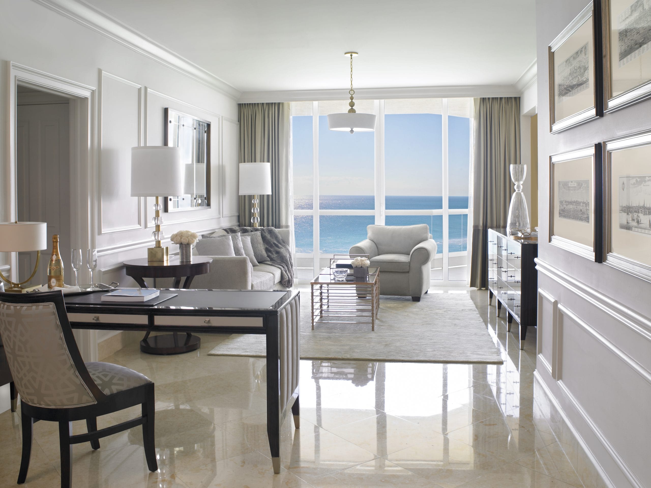 Luxury oceanfront suite featuring an elegant living area, marble flooring, designer furnishings, and floor-to-ceiling windows with panoramic Atlantic Ocean views at Acqualina Resort Miami Beach.