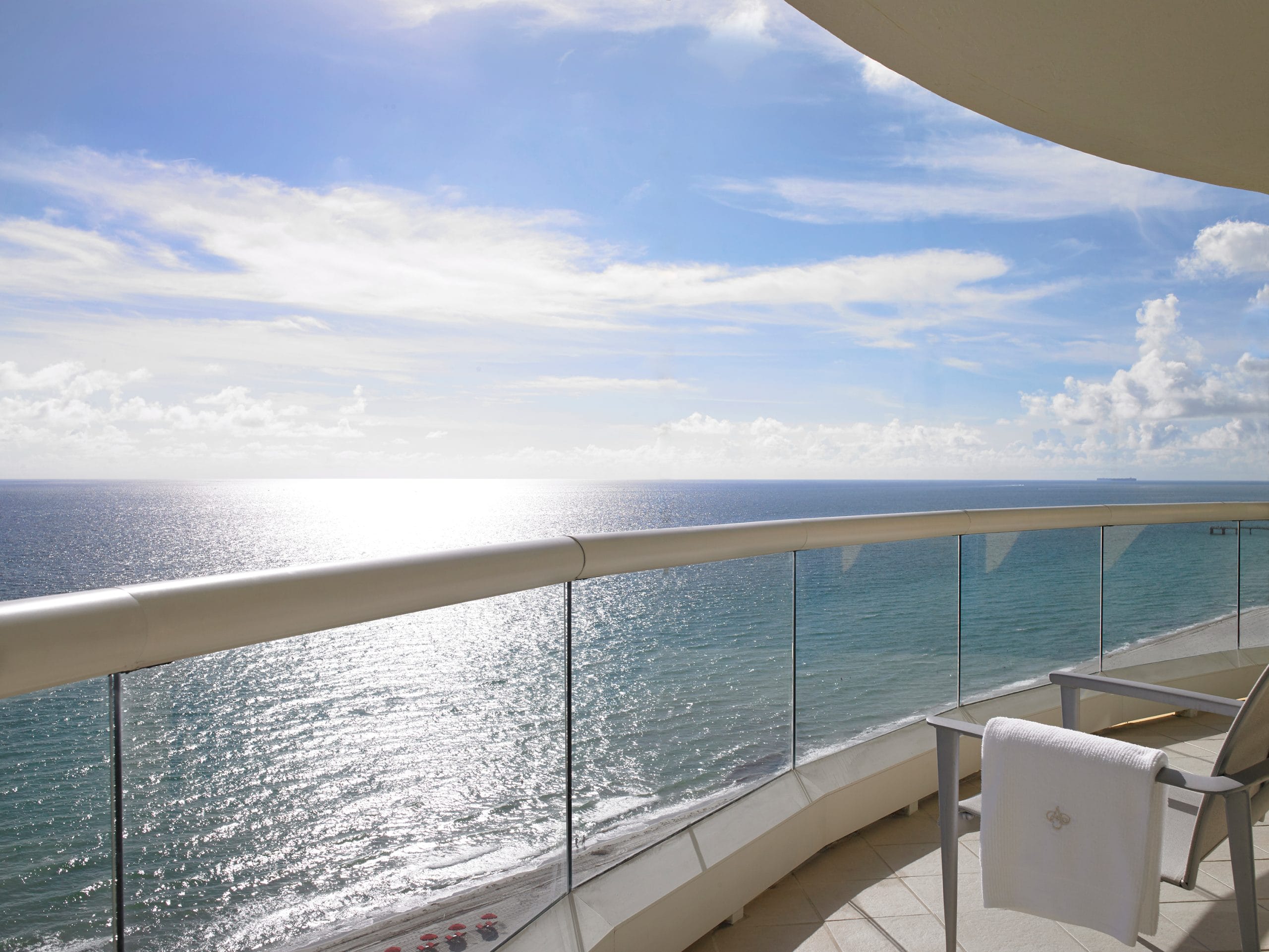 Private oceanfront balcony featuring outdoor seating, glass railings, and panoramic views of the Atlantic Ocean at Acqualina Resort Miami Beach.