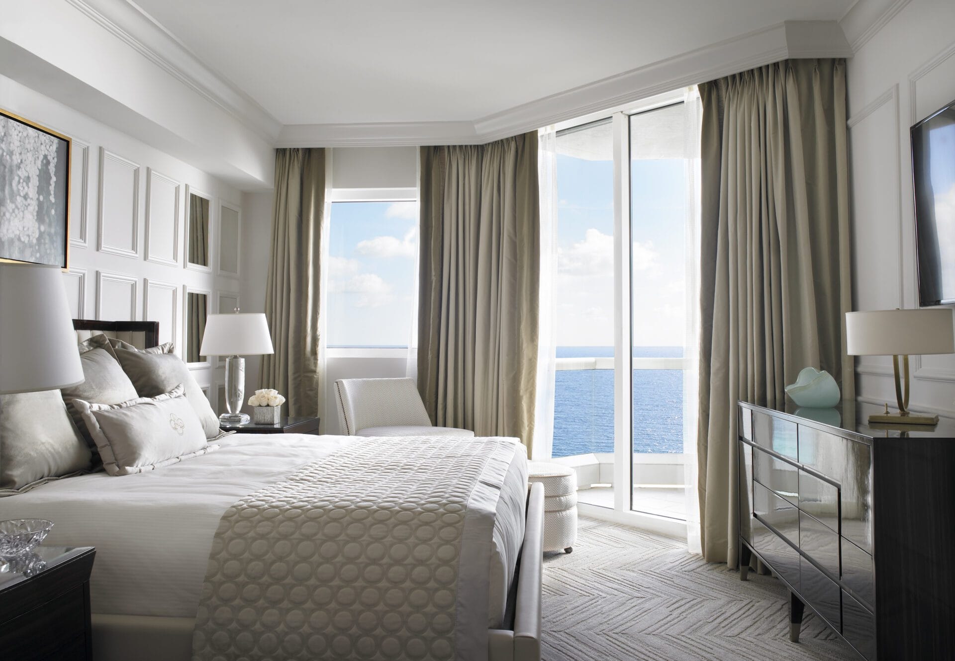 Luxury oceanfront suite bedroom featuring a plush king bed, elegant furnishings, floor-to-ceiling windows, and panoramic Atlantic Ocean views at Acqualina Resort Miami Beach.