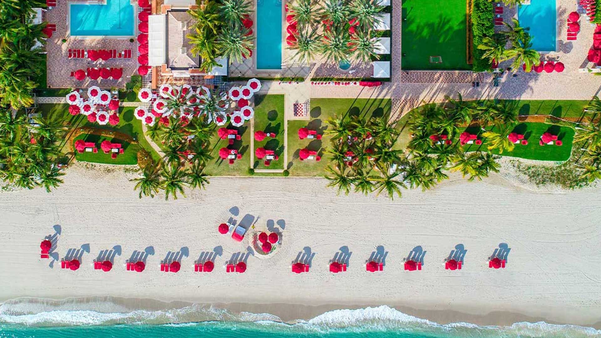 aerial view of luxury beachfront resort with red umbrellas and palm trees