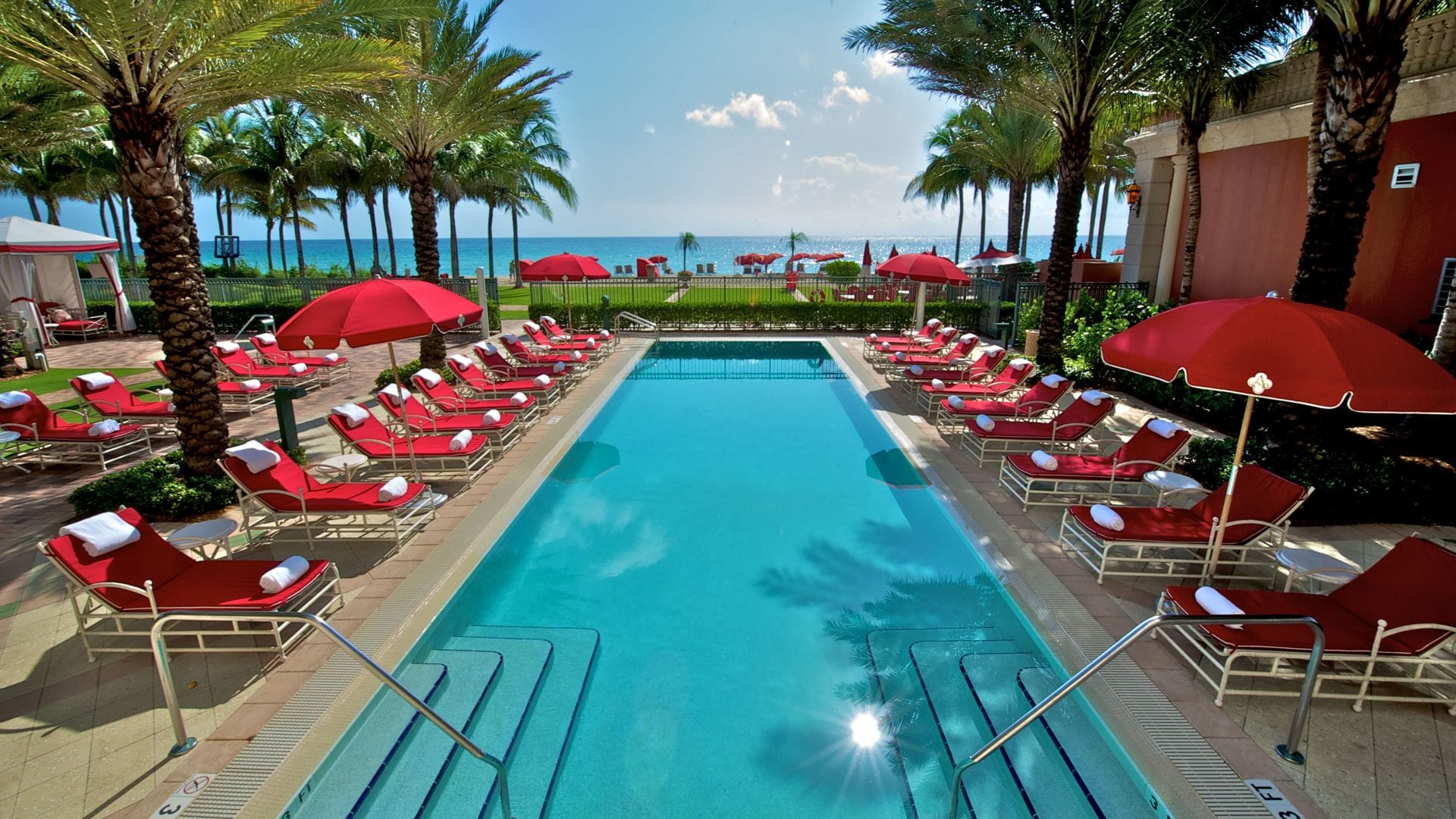 luxury resort pool with red lounge chairs and ocean view