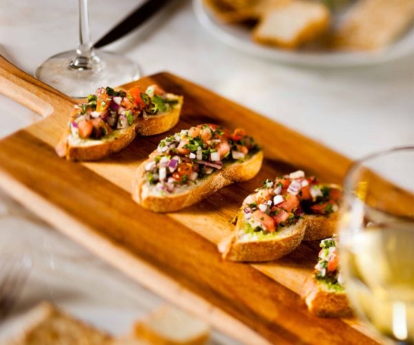 Bruschetta appetizers with tomato, herbs, and diced vegetables served on a wooden board